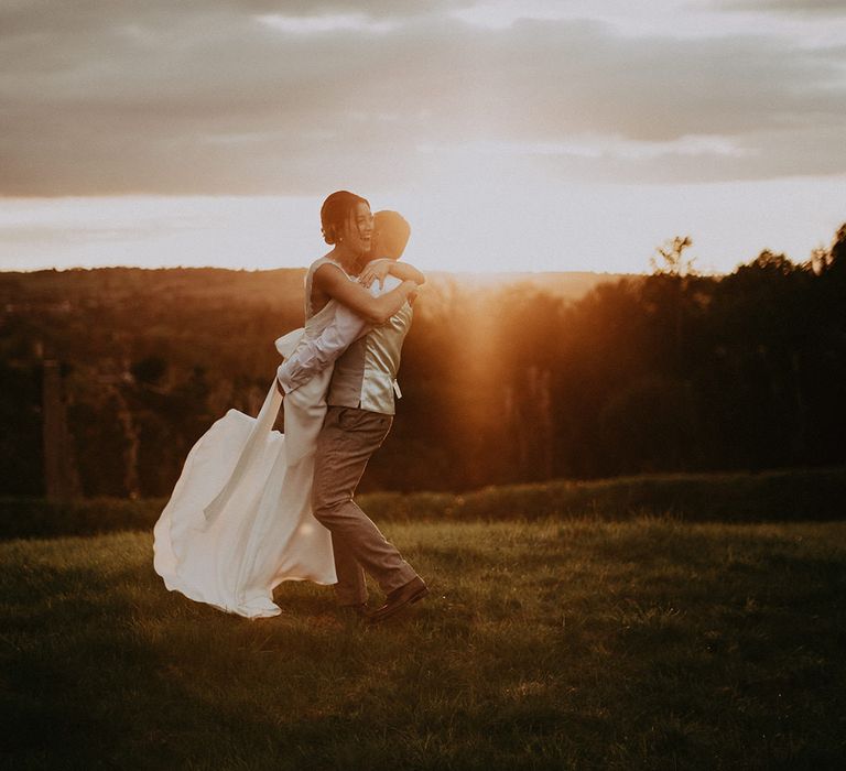 Groom lifts his bride outdoors during golden hour portraits 