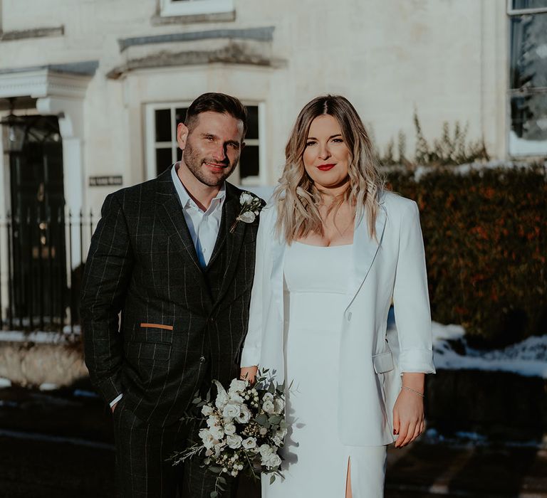 Bride in white wedding dress with split leg and ruffle detail and blazer with the groom in dark grey groom outfit for Christmas registry office wedding 