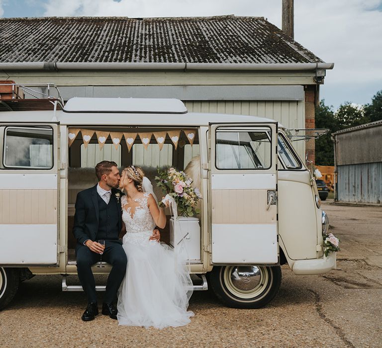 Bride in lace Dando London wedding dress kissing the groom in a navy suit as they sit in the cream VW wedding transport 