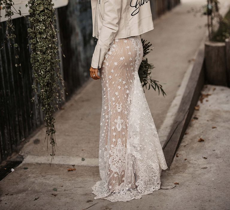 Bride in fitted lace wedding dress wearing cream leather jacket with personalised with her new last name on the back 