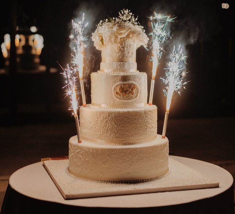 Four tier buttercream wedding cake with mini sparkler decorations, white flower wedding cake topper and intricate detailing 