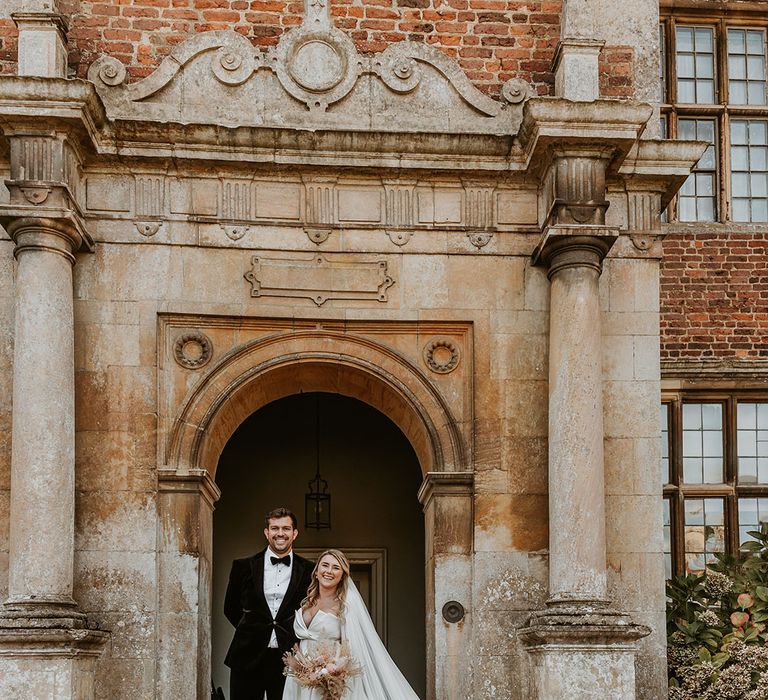 Doddington Hall and Gardens country house in Lincolnshire with the groom in traditional black tie and the bride in a luxe wedding dress with floral embroidered veil 