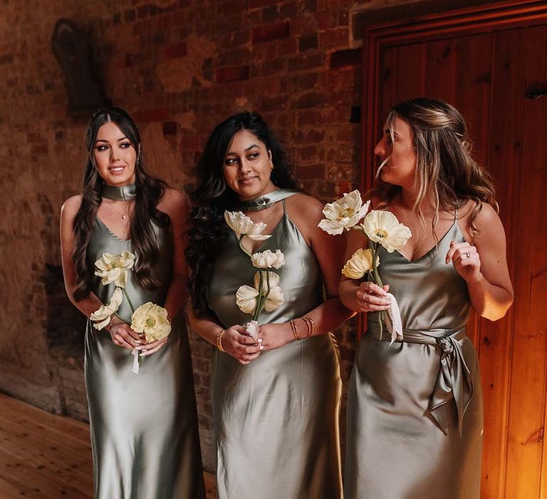 Bridesmaids in green mismatched bridesmaid dresses holding mini yellow and white bouquets 