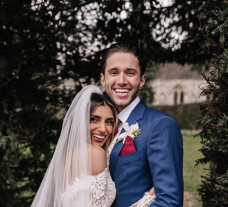 Groom in blue suit with red tie and pocket sqaure embracing the bride in a long sleeve off the shoulder sparkly wedding dress 