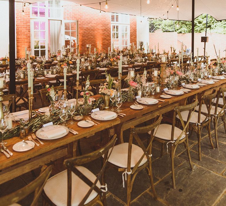 Marquee wedding breakfast with light blue taper candles, pink and peach flowers and festoon and fairy lighting for decorations 