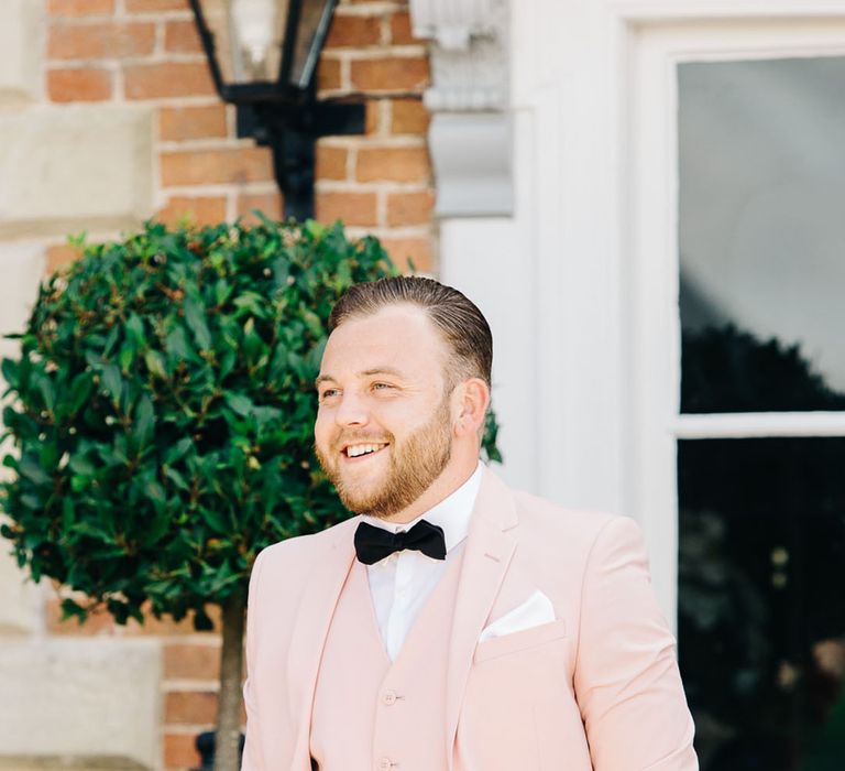 Groom in light pink wedding suit with black bow tie for wedding day 