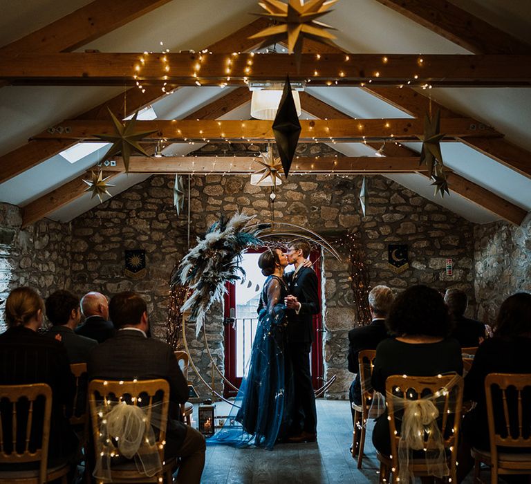 The bride and groom share their first kiss as a married couple in front of the pampas grass moon gate decoration 