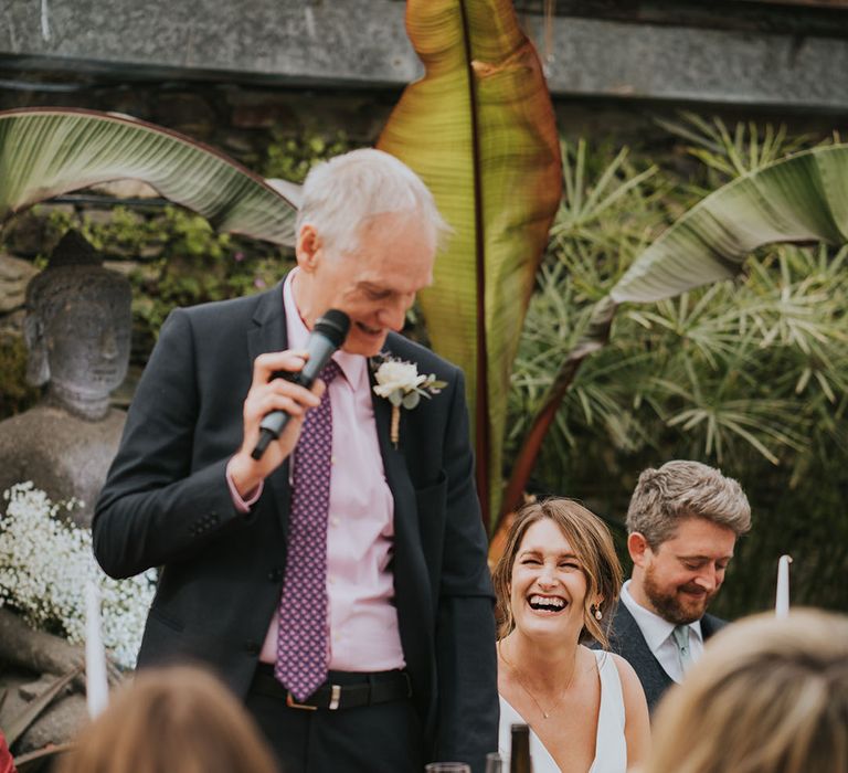 The father of the bride wearing a pink shirt and patterned tie reads out his speech 