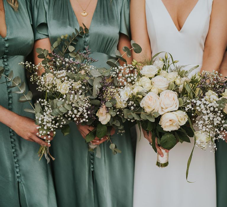 Bride in plunging wedding dress wearing white rose bouquet with the bridesmaids wearing short sleeve green bridesmaid dresses holding matching bouquets 