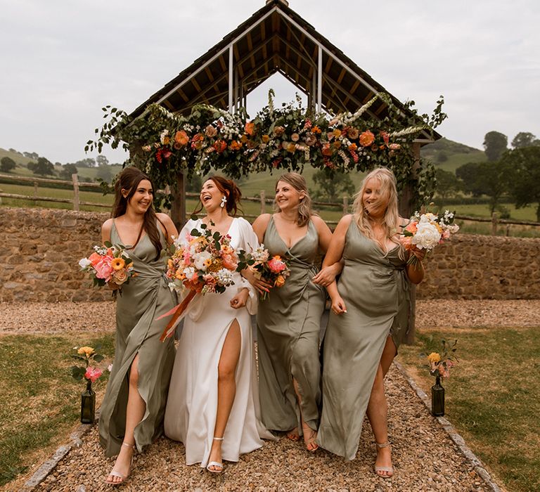 Fun wedding party photo with the bridesmaid in green wrap dresses holding orange wedding bouquets 