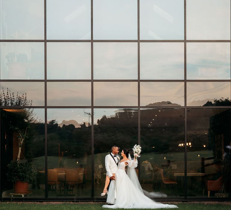 Bride and groom poses in front of large window at crumplebury wedding venue