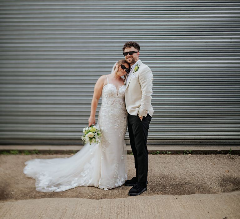 Bride in lace wedding dress with groom in beige suit with black sunglasses 