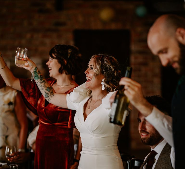 The bride drinks at the wedding breakfast wearing a fitted wedding dress 