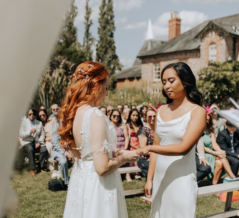 Two brides stand together in white wedding dresses for their same sex wedding ceremony 