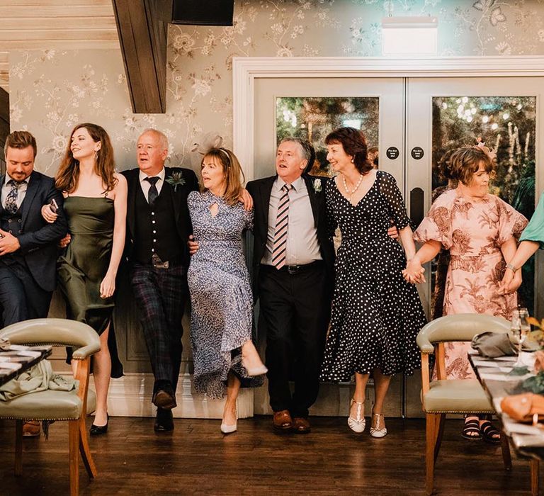 Wedding guests dancing a wedding reception by linking arms with each other 