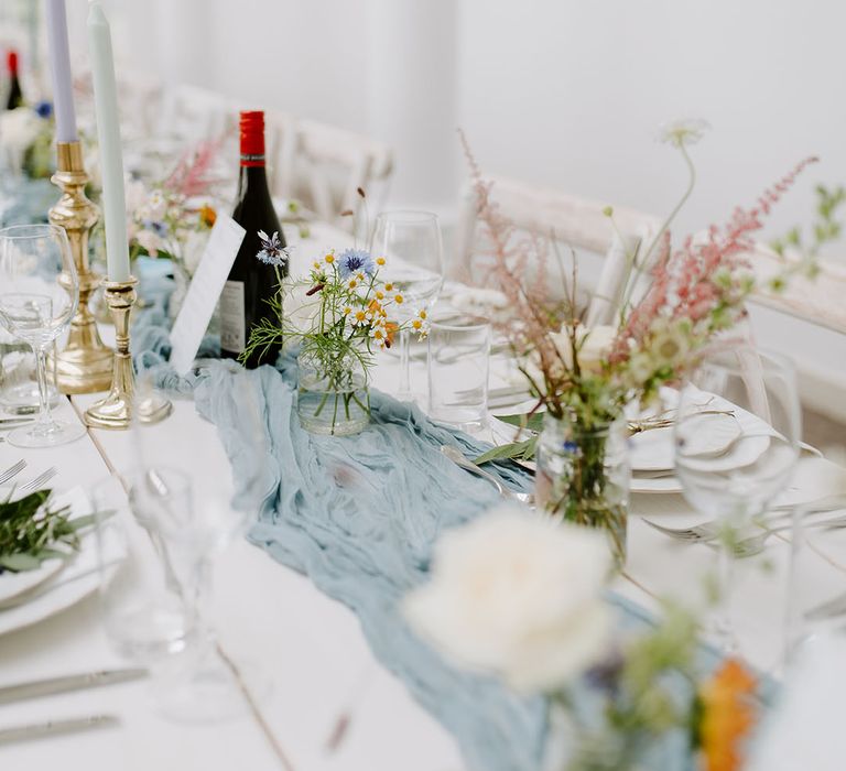 Bud vases with pastel wedding flowers with dusty blue table runner on long banquet tables 