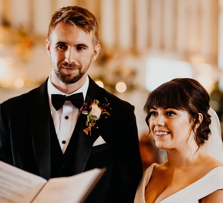 Groom in black tuxedo smiling with bride in off the shoulder wedding dress 