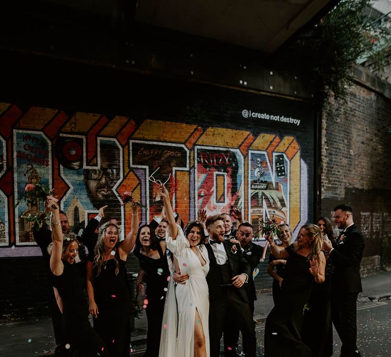 Bridal party wearing sleek black bridesmaid dresses with the bride wearing a puff sleeve front slit wedding dress 