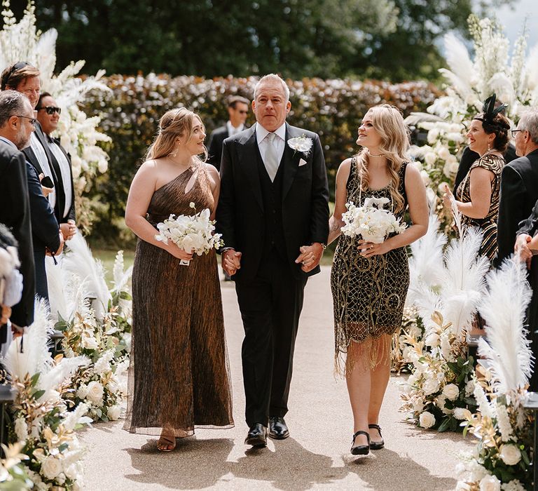 Groom walks down the aisle with his daughters in gold outfits 