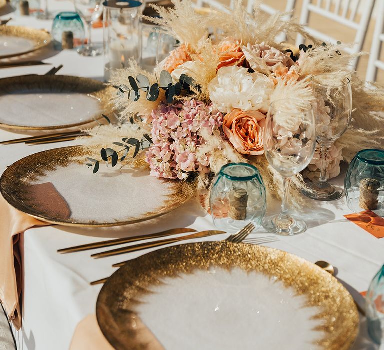 Pampas grass with peach and pink flowers as table centrepieces with white and gold charger plates 