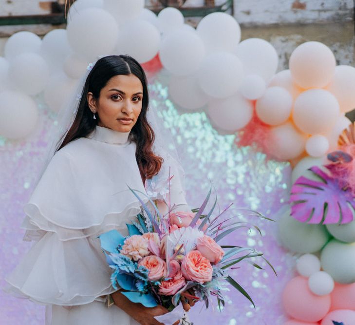 Bride in short wedding dress and boots holding her holographic pastel bouquet 