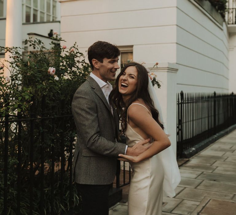 Bride in slip wedding dress laughing during urban couples portraits 