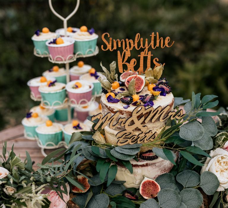 Wedding cake and cupcakes on wooden table with foliage decoration 