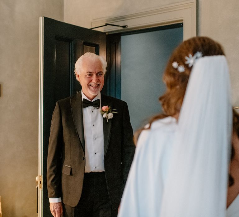 Father of the bride smiling as he see's his daughter for the first time on her wedding day. Wearing a black bow tie and pink rose button hole flower