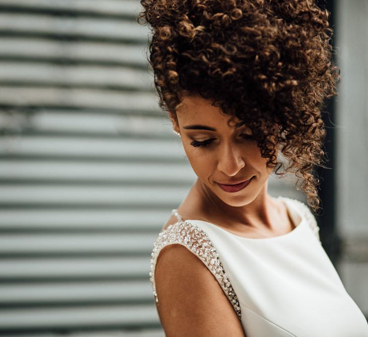 A bride with curly hair smiles over her shoulder