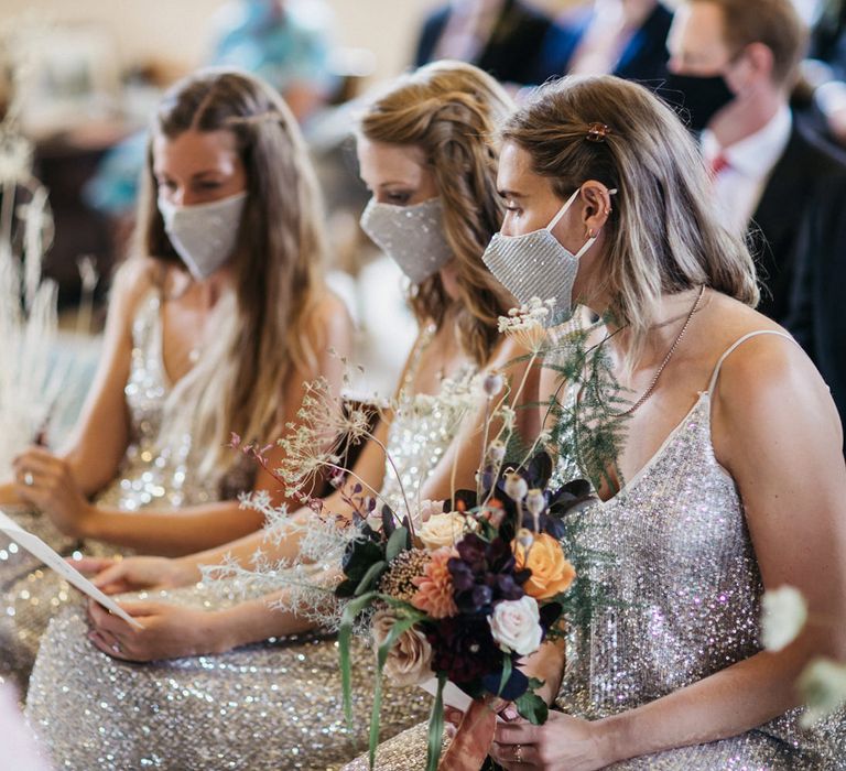 Bridesmaids in silver sequin dresses and matching facemarks sitting in the church 