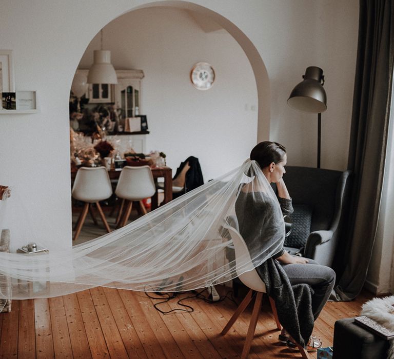 Woman holding out bride's cathedral length veil as she sits looking out the window