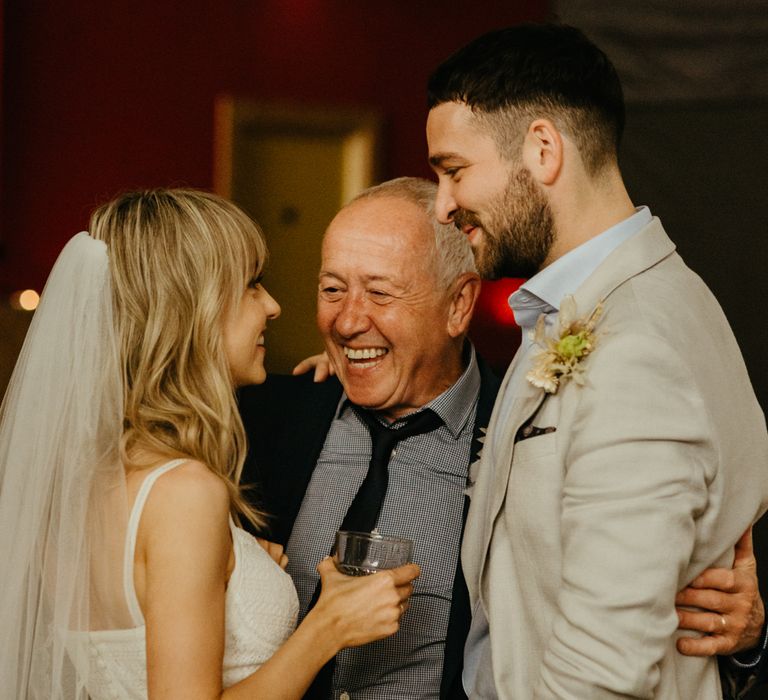 Bride and groom are hugged by smiling brides father