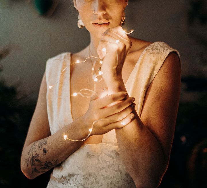 Bride in a crown and fitted wedding dress with jacquard detail holding a string of fairy lights 