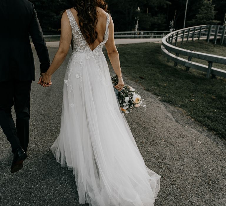 Bride & groom hold hands as they walk together 