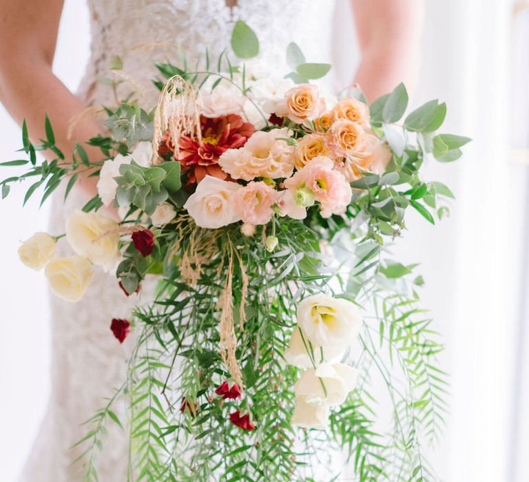 Bride holding bouquet of blush roses, carnations and wild foliage