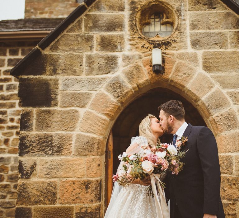 Bride and groom kissing outside their church wedding