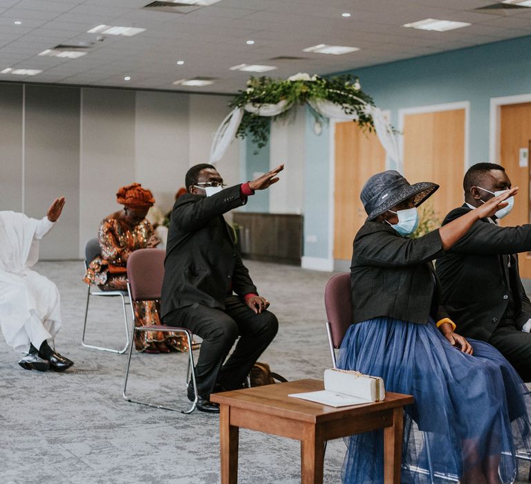 Guests in face masks sit socially distanced saluting the bride and groom at Bridge Community Church wedding