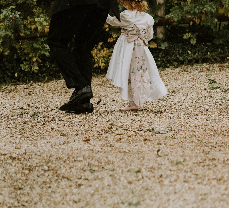 Flower girl in white satin dress with floral bow and flower crown 