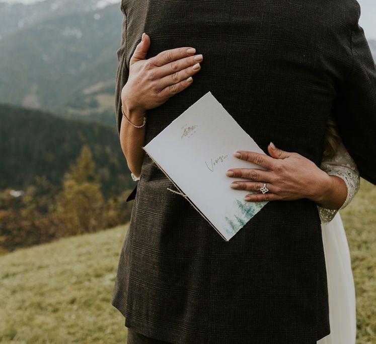 Bride embracing her husband clutching a vow booklet with tree design