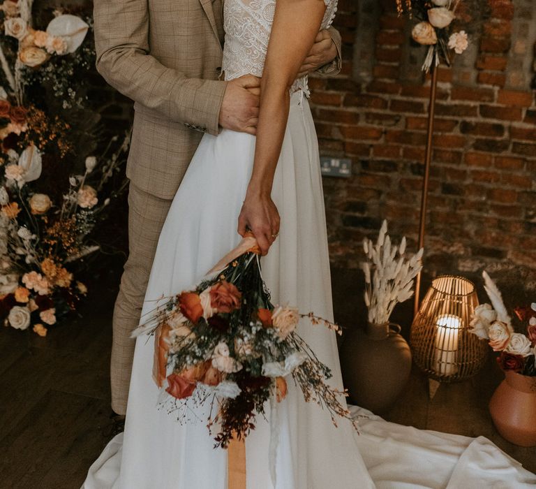 Bride with curly wedding hair hugging groom in casual beige suit for rustic barn wedding