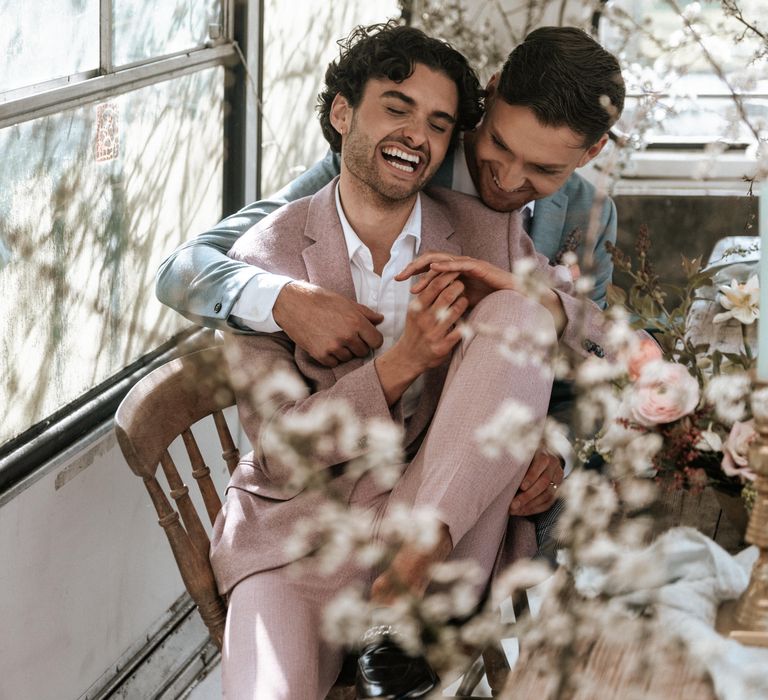 Grooms sit beside rustic and pastel coloured floral bouquets with wooden twisted vines 