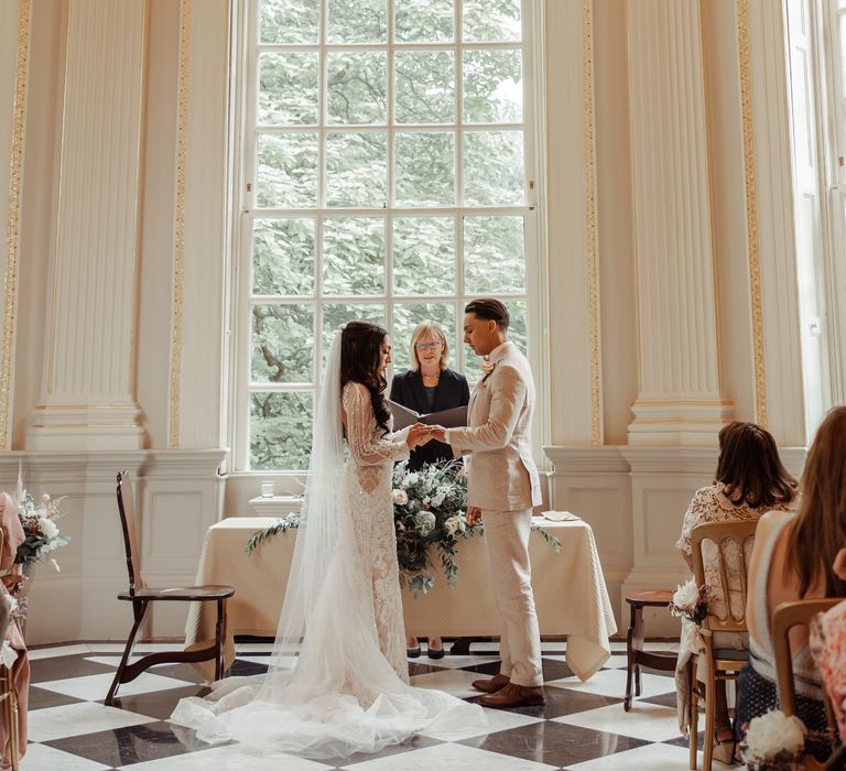 Bride & groom stand in front of large window during wedding ceremony