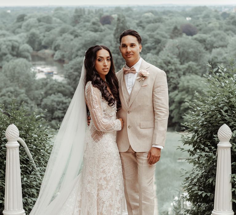 Bride & groom pose outdoors as groom wears pastel coloured suit 