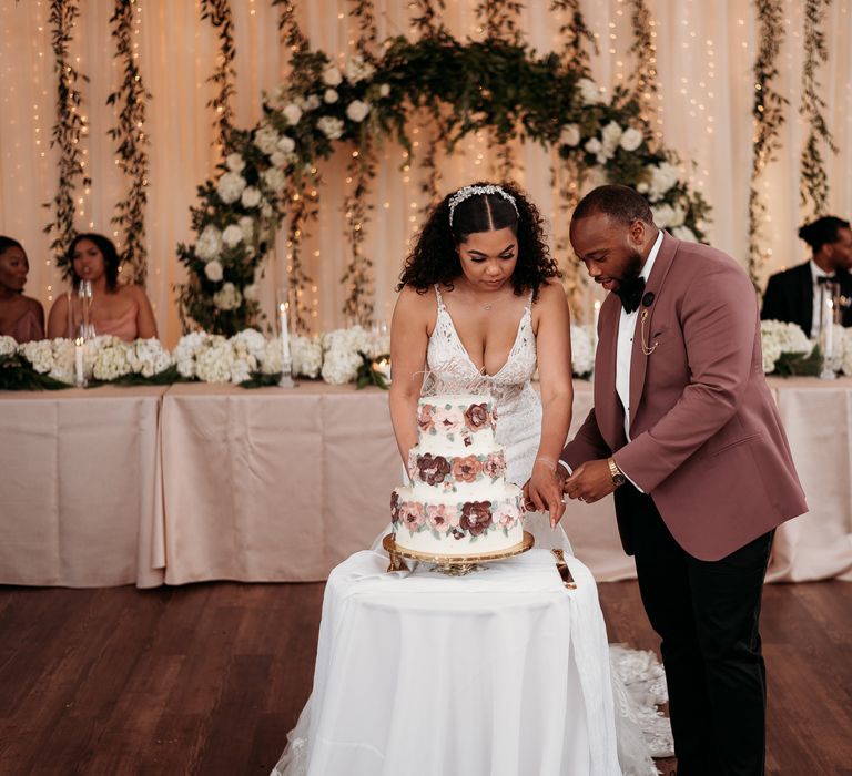 Bride & groom cut their wedding cake in front of floral wedding arch