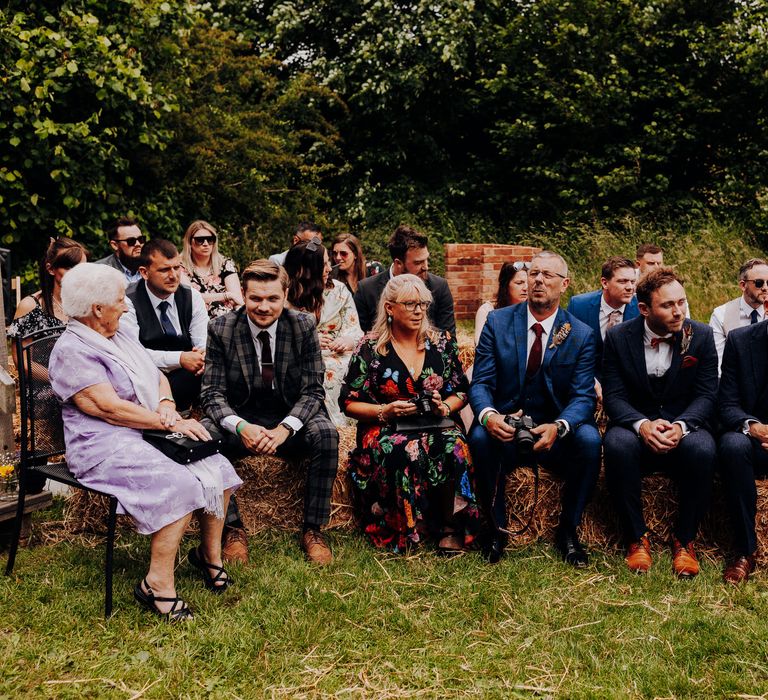 Wedding guests sit together on hay bales before wedding ceremony 