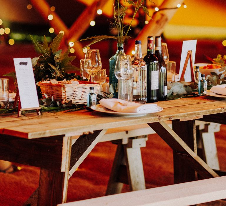 Wooden table sits within tipi as gin bottles are used as vases