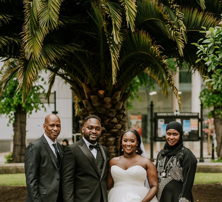 West African bride & groom stand with their family outdoors for black tie wedding at Core Clapton