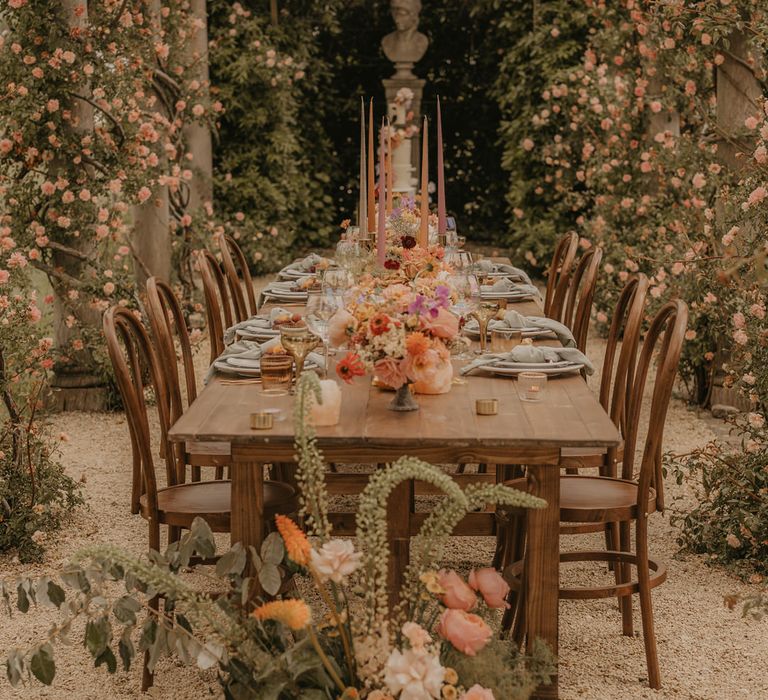 Outdoor wedding reception at Euridge Manor with tall coloured taper candles in gold candlesticks surrounded by pastel orange wedding flowers 