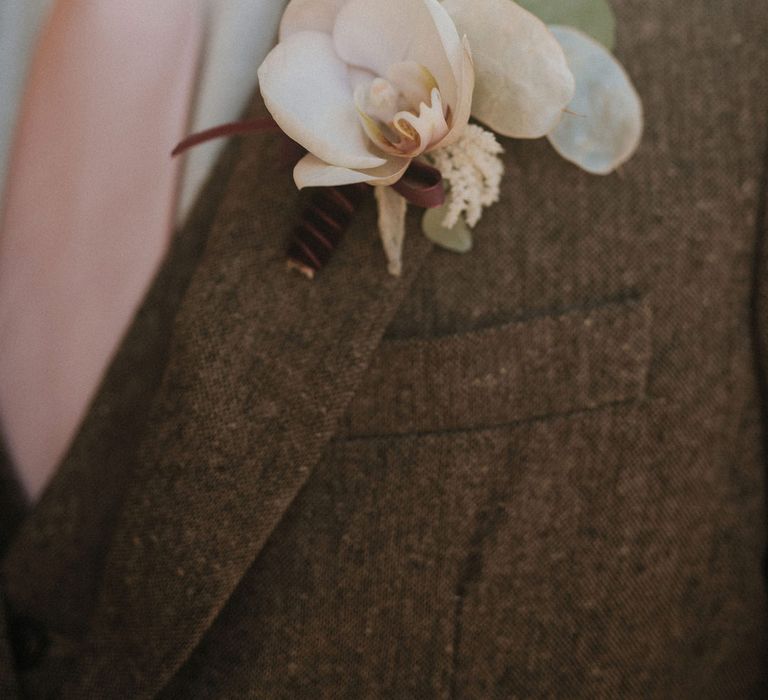 Groom in a brown suit and pale pink tie with an orchid groom buttonhole