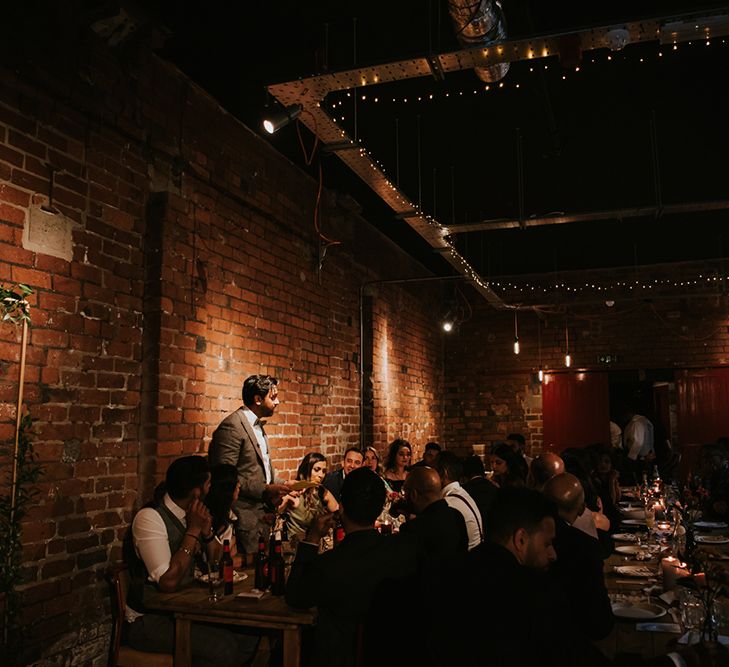 A groom stands to make a speech at industrial wedding venue.